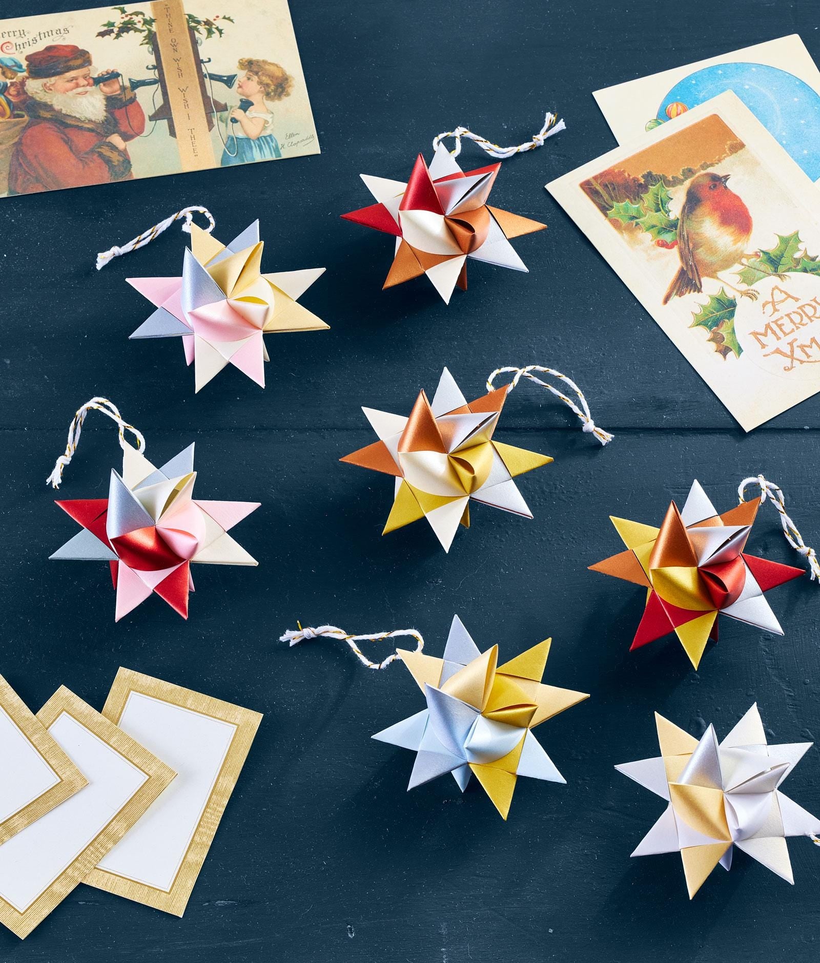 Colorful paper star ornaments on a dark surface with Christmas cards in the background.